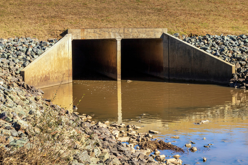Culvert opening with brown water surrounded by rocks